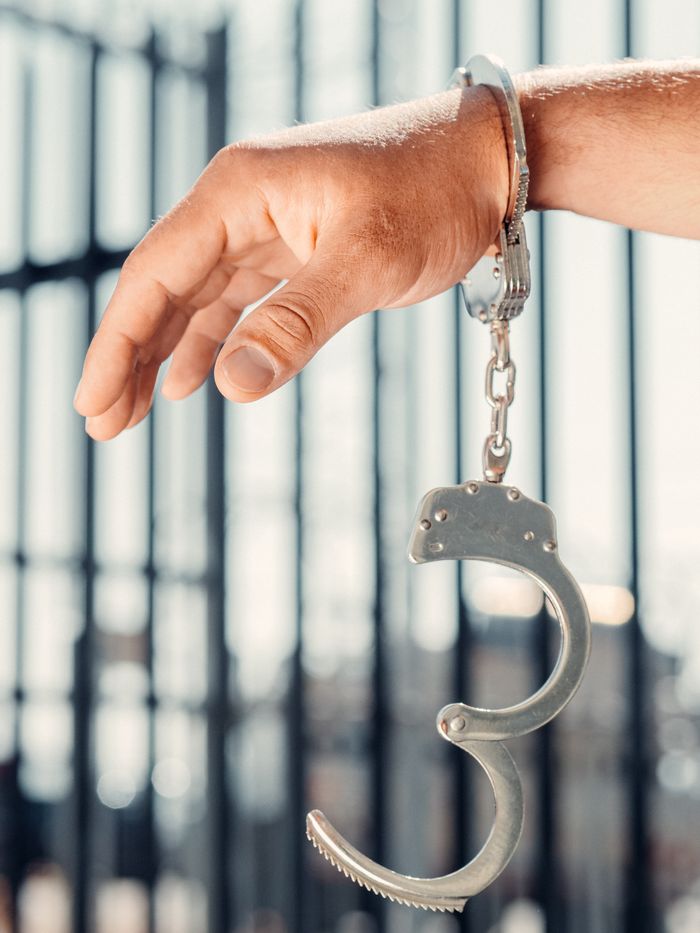 contact-img A close-up, conceptual shot of a handcuffed hand with one open handcuff against blurred bars.